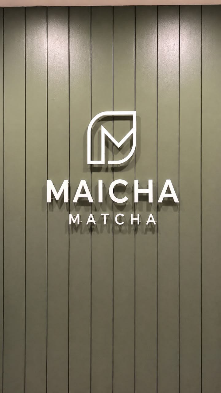Maicha Matcha white dimensional logo and letters mounted on an olive slatted interior wall