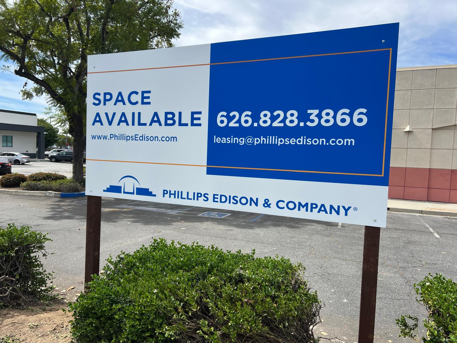 Phillips Edison & Company Space Available leasing sign on posts in a retail center parking lot