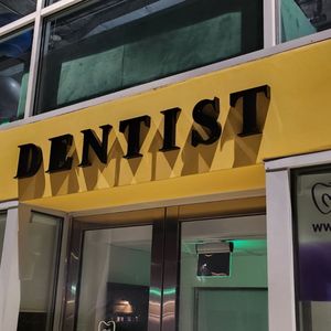 Black dimensional DENTIST letters mounted on a yellow storefront awning