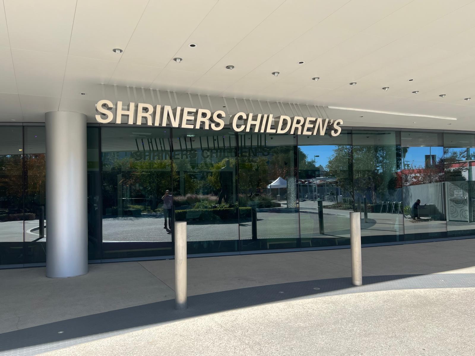 Shriners Children's brushed aluminum channel letters mounted above the glass entrance of the medical center